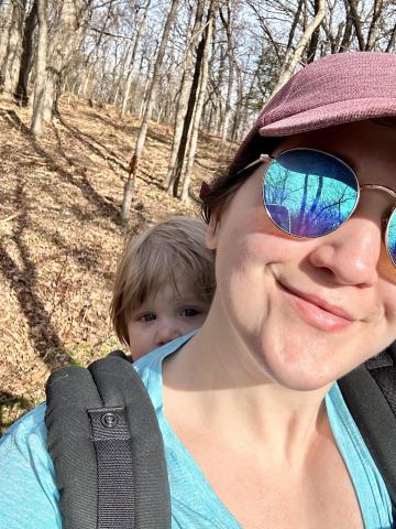 戴着墨镜和红帽的女人背着背着婴儿的背包在树林里徒步旅行
