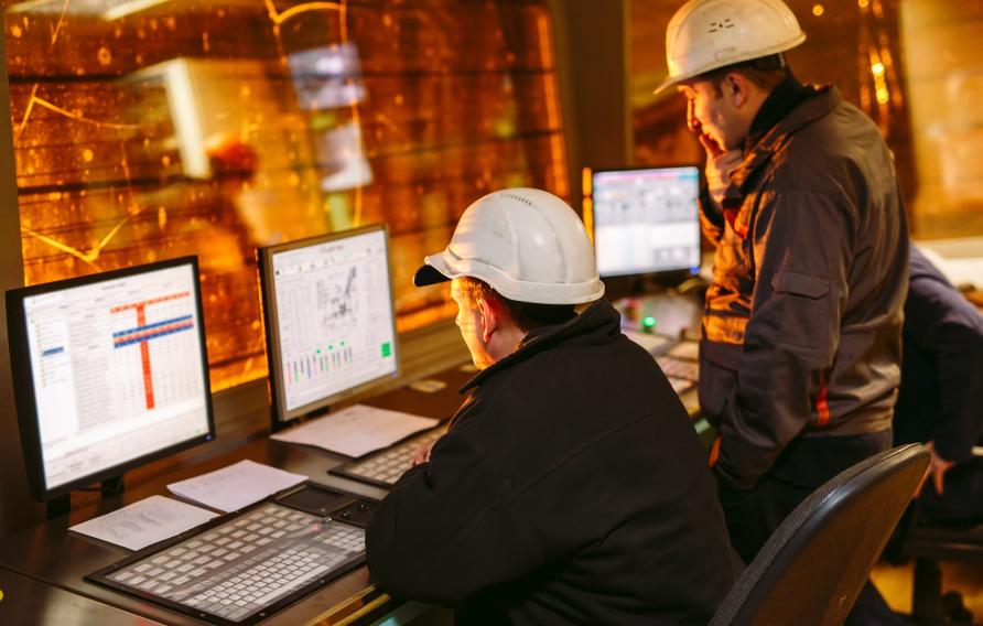 Two people wearing helmets looking at computers