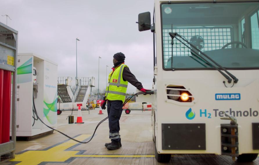 Man in hi viz yellow waistcoat refueling a luggage tug at an airport.