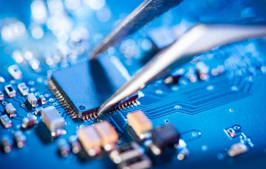  Electronic technician holding tweezers and assemblin a circuit board.