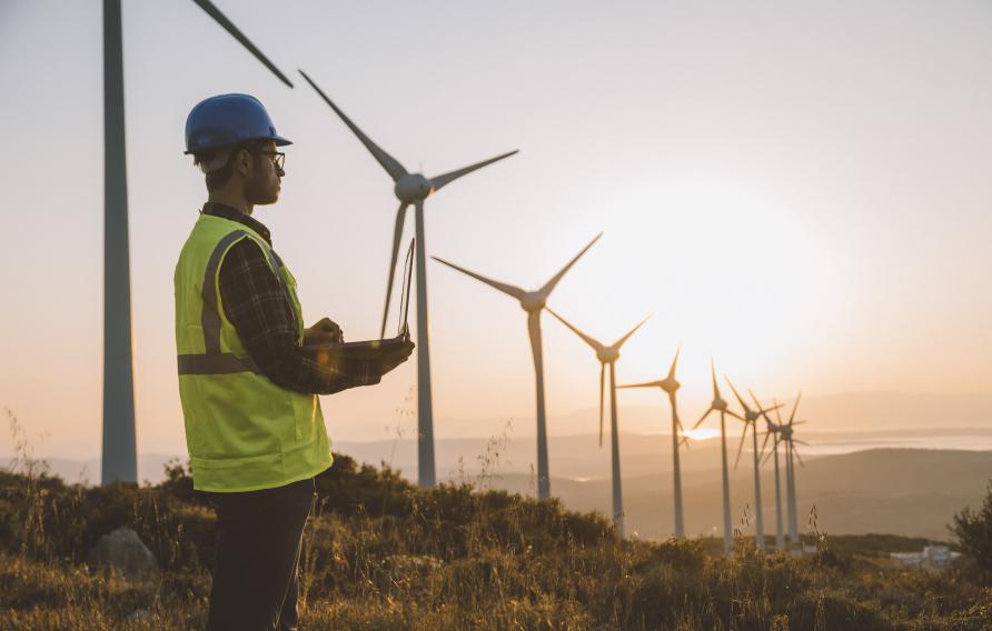 Silhouette of young male engineer holding laptop computer planning and working for the energy industry and standing beside a wind turbines farm power station at sunset time. XXXL size taken with Canon 5D MIV