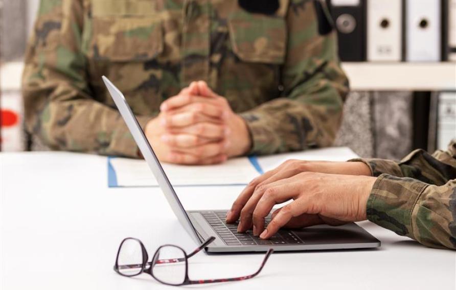 Military officers meet to discuss recruitment. They are using a laptop.