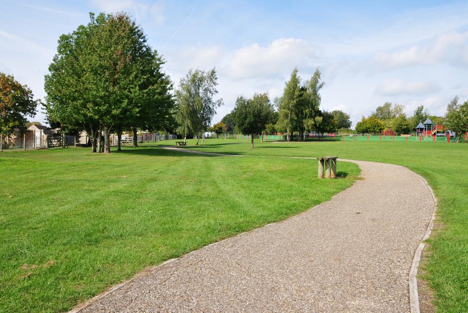 Green park with path, trees, green grass and playground.