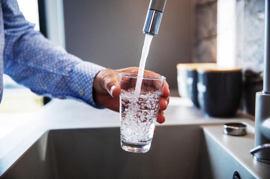 Man in blue dress shirt fills glass with tap water