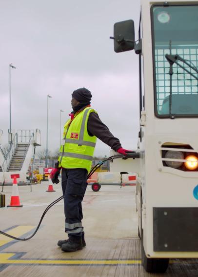 Man in hi viz yellow waistcoat refueling a luggage tug at an airport.